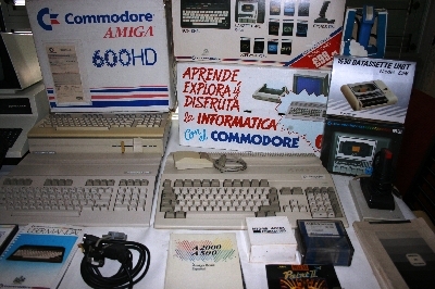 Commodore Amiga 600HD (en su caja), caja del Plus/4, Commodore 64C (segunda unidad, en su caja), Commodore 128D, Commodore 128 y Commodore Amiga 500 Plus, unidades de casete 1530 y 1531, joysticks, manuales, software y cables